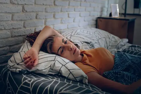 Eine Frau liegt im Bett, ihr Blick ist müde und nachdenklich. Sie kämpft mit den Symptomen eines Fatigue-Syndroms.