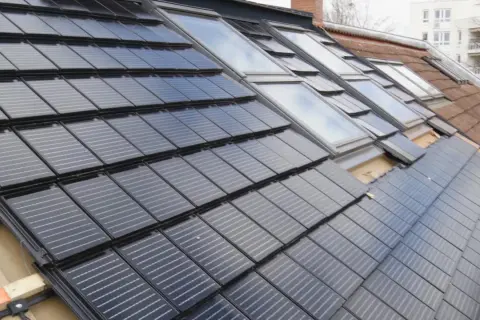 Dach renovieren kosten: Solarmodule werden auf einem Dach mit Dachfenstern installiert.