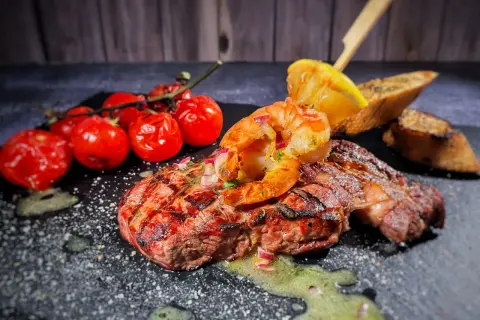 Perfektes Surf and Turf Rezept: saftiges Steak mit gegrillten Garnelen, Kirschtomaten und Zitronenspalte auf schwarzem Stein.