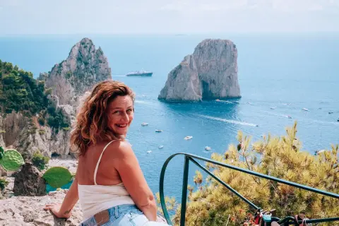 Donna sorridente con vista sui Faraglioni e il mare azzurro, un ricordo dalla spiaggia di Marina Piccola.