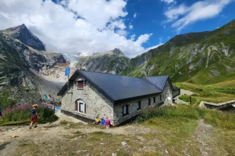 Kamienny schron na GR20 Korsyka, z lodowcem w tle i zielonymi górami.