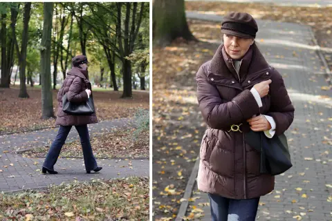 Kobieta w brązowej kurtce na zimę spaceruje po parku jesienią.