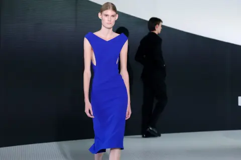 Modella con abito blu elettrico, un'opera di Simone Bellotti, sfila su una passerella minimalista.