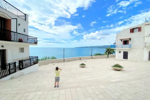 Bambino ammira il mare azzurro dalla piazzetta Petrone a Vieste, con case bianche e cielo nuvoloso.