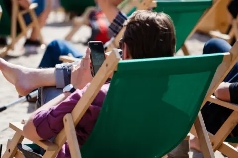 Mężczyzna w okularach przeciwsłonecznych relaksuje się na leżaku, przeglądając telefon. Idealny urlop wypoczynkowy.