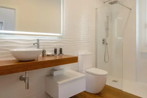 Baño moderno con lavabo sobre mueble de madera, inodoro y ducha con mampara de cristal. Perfecto para impermeabilizar ducha y mantener la limpieza.