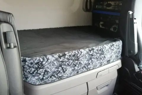 L'intérieur d'un camion Scania, prêt pour la nuit. Le lit est fait, avec une housse au motif abstrait gris et noir, parfait pour le scania tuning nuit.