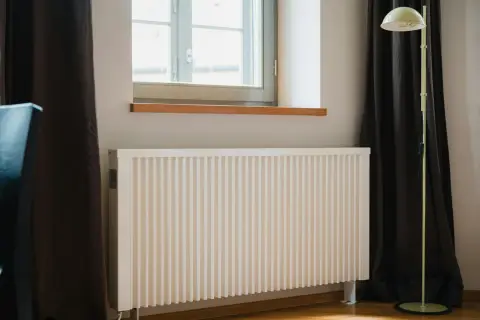 Vitt element med ribbad front, perfekt för att bygga elementskydd. En golvlampa står bredvid.