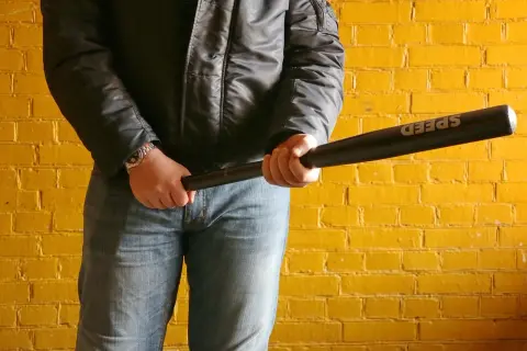 Mężczyzna w czarnej kurtce i jeansach trzyma kij baseballowy z napisem "SPEED". Groźny rozbój wisi w powietrzu.