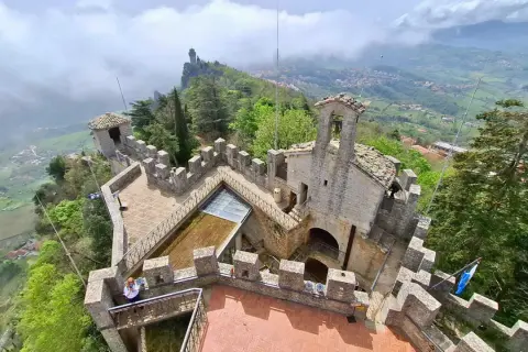 Widok z góry na kamienne fortyfikacje i wieże podczas san marino roaming. W oddali widać mgliste wzgórza i miasteczko.