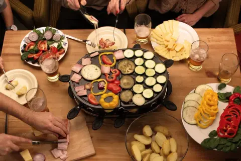 Mesa con raclette, quesos, patatas, ensalada y muchas verduras para raclette: pimientos, calabacín, berenjena y tomate.