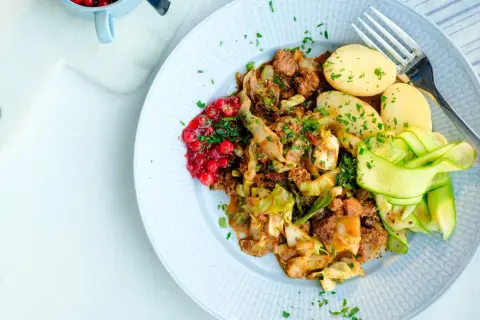 En tallrik med stuvad vitkål, köttfärs, kokt potatis, gurkband och rårörda lingon. Ett härligt kålmaja recept för en smakrik middag.