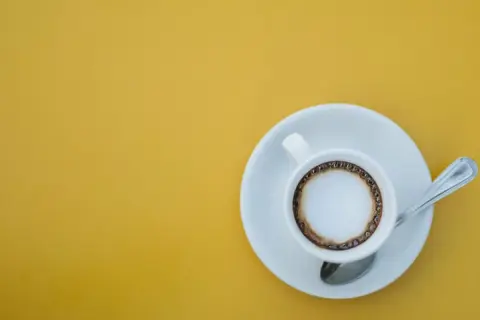 En vit kopp med kaffe macchiato står på en tefat med en sked. En perfekt start på dagen, det är vad macchiato betyder.