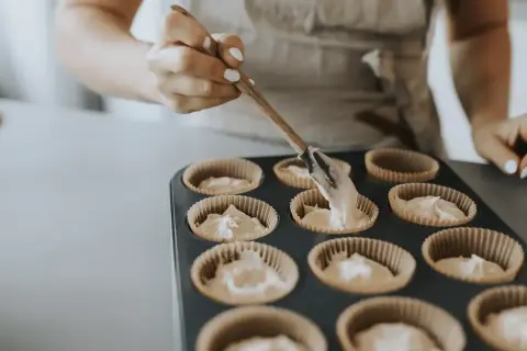 En person fyller muffinsformar med smet. Bra baka tips för perfekta muffins.
