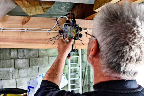 Elektryk kończy instalację elektryczną w garażu, łącząc przewody w puszce.