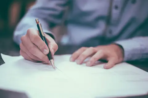 Dłoń pisze długopisem na dokumencie. Może to być umowa, faktura, a nawet wypełnianie wniosku o nip-8.