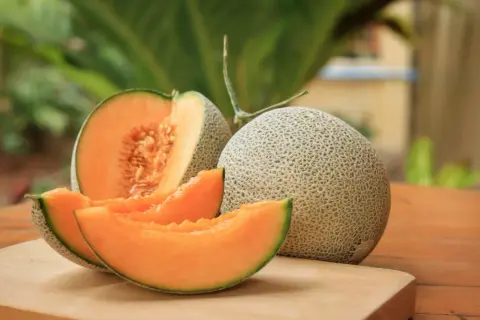 Melón entero y cortado, mostrando su pulpa naranja y semillas. Un festín de las propiedades del melón.