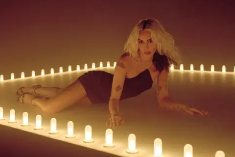 Miley Cyrus w stylizacji na "endless summer vacation" leży wśród rozświetlonych lamp.