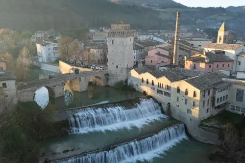 Cascata e ponte ad arco a Fermignano, vicino Urbino, con edifici storici e una ciminiera.