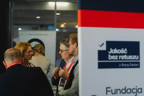 Ludzie rozmawiający na tle banera z napisem "Jakość bez retuszu".