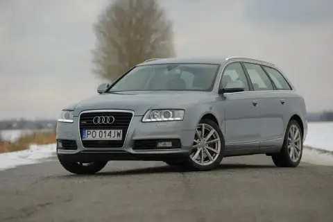 Szary Audi A6 C6 kombi na drodze. Zbliżenie na przód auta, widoczne światła, grill i tablica rejestracyjna. Wymiary tego modelu są idealne dla rodziny.