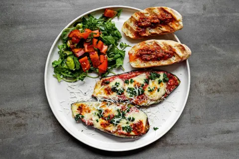 Gegrillte Auberginenhälften mit geschmolzenem Käse, Bruschetta und einem frischen Salat – perfekt für einen italienischen Abend.