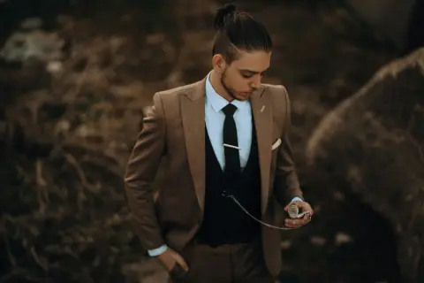 Stilberatung für Senioren: Mode ab 60. Ein Mann im eleganten braunen Anzug mit Weste und Krawatte hält eine Taschenuhr.