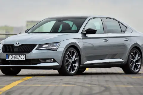 Elegancki, szary Skoda Superb 2024 z czarnym dachem i przyciemnianymi szybami, zaparkowany na parkingu.
