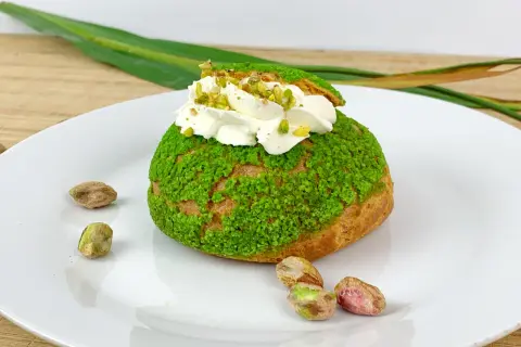 Pyszne ptysie z kremem pistacjowym, posypane zielonymi okruszkami i orzechami.