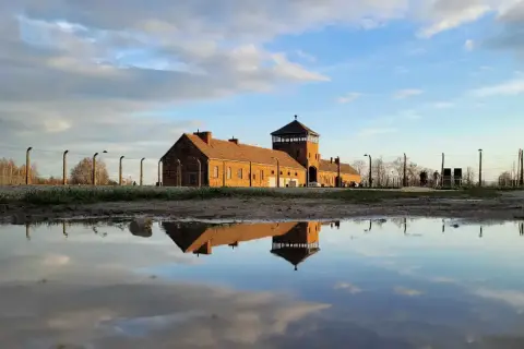 Odbicie ceglanego baraku z wieżą strażniczą w kałuży. To miejsce, gdzie jest Auschwitz, przypomina o historii.