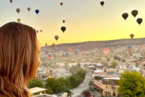 Kvinna ser på en magisk soluppgång över Kappadokien, Turkiet, med hundratals luftballonger som svävar i den gyllene himlen.