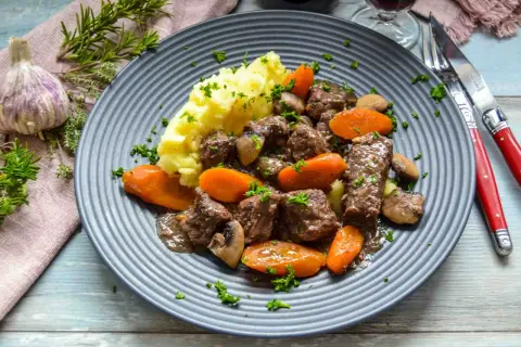Herzhaftes Boeuf Bourguignon Rezept: zartes Rindfleisch mit Karotten, Pilzen und Kartoffelpüree auf einem grauen Teller, garniert mit Petersilie.