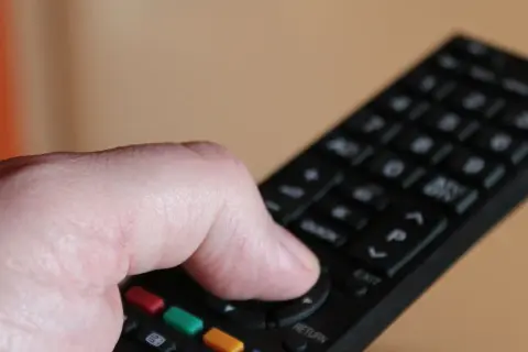 Dłoń naciska przycisk na pilocie, by dowiedzieć się, jak odbierać wszystkie kanały telewizji naziemnej.