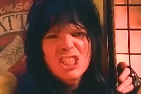 Rockman z lat 80. z burzą czarnych włosów i wykrzywioną twarzą, jakby śpiewał głośno utwory lat 80.