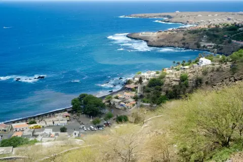 Vue d'un village côtier au Cap-Vert, avec des maisons blanches et colorées nichées sur une colline. Le nom de famille cap verdien résonne dans l'air salin.