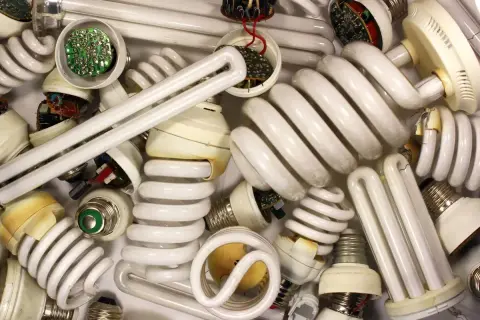 Stos zużytych żarówek energooszczędnych, w tym spiralnych i prostych jarzeniówek, z widocznymi elementami elektronicznymi.