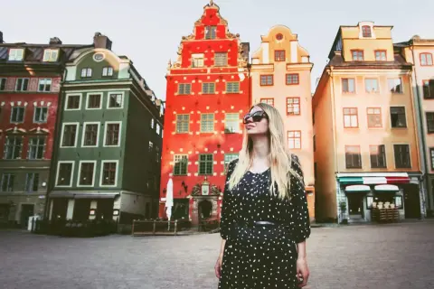 En kvinna med solglasögon står framför färgglada hus på ett torg. Kanske är detta sveriges vackraste stad.