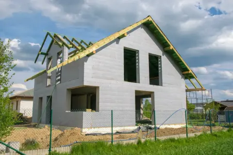 Dom w budowie, z widoczną konstrukcją dachu i pustymi otworami okiennymi. Zastanawiasz się, ile trwa budowa domu? Ten etap to dopiero początek.
