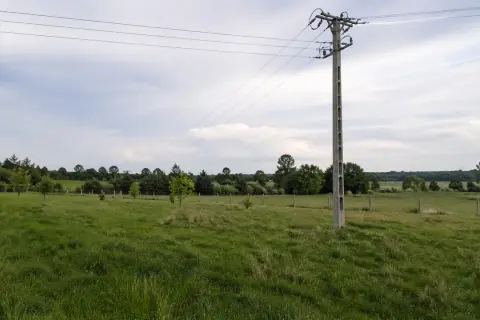 Słup na działce ponad 30 lat, stoi pośród zielonej łąki, z liniami energetycznymi biegnącymi ku horyzontowi.