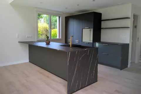 Îlot de cuisine moderne avec plan de travail en marbre noir veiné d'or. Ce modèle de cuisine simple, aux lignes épurées, est complété par des meubles sombres et un robinet doré.
