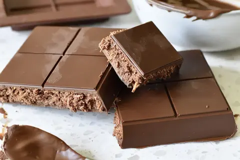 En fransk chokladtårta med krispigt fyllning, uppdelad i bitar. En sked med chokladkräm syns i förgrunden.