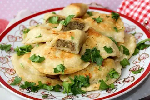 Talerz pełen złocistych pierogów z soczewicą, udekorowany świeżą natką pietruszki. Idealne na obiad!
