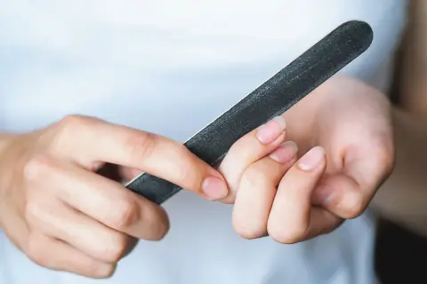 Dłonie z naturalnymi paznokciami, które są piłowane pilniczkiem. Zastanawiasz się, ile warstw ma paznokieć?