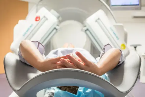 Pacjent leży w aparacie do scyntygrafii, ręce splecione na piersi.