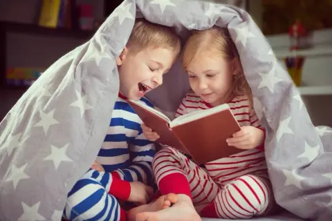 Chłopiec i dziewczynka pod gwiazdkową kołdrą czytają książkę. To idealny wiersz na dobranoc dla chłopaka, pełen przygód i śmiechu.