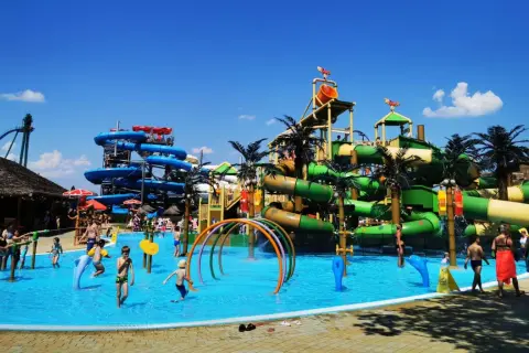 Wesoły wodny park rozrywki z mnóstwem zjeżdżalni, basenów i palm. Dzieci bawią się w wodzie, ciesząc się letnim dniem.