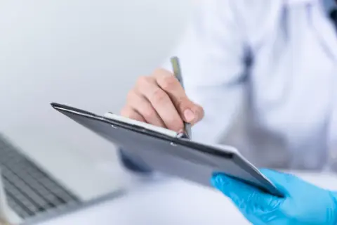 Lekarz w niebieskich rękawiczkach notuje wyniki badań, w tym poziom kalprotektyny w kale, na tablecie.
