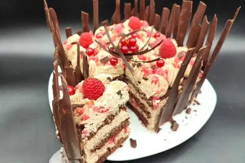 Una golosa torta cioccolato e lamponi, decorata con panna, frutti rossi e scaglie di cioccolato. Una fetta è già stata servita.