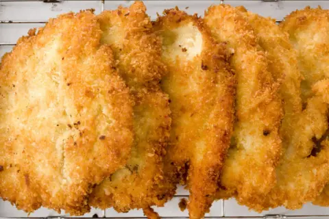 Fileteadas pechugas de pollo empanadas, doradas y crujientes, reposan sobre una rejilla metálica.