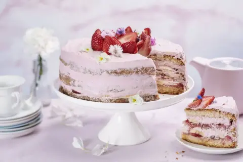 En vacker jordgubbstårta med rosa frosting, dekorerad med färska jordgubbar och blommor. Perfekt för ett somrigt fika, kanske inspirerad av ett enkelt jordgubbstårta recept.